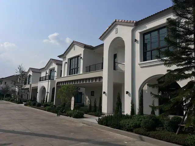บ้านเดี่ยวสีขาวในโครงการ บัวเชิงชายและกรอบซุ้มโค้งแนวเดียวกันทั้งแถว